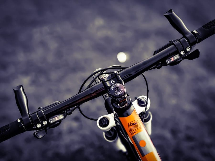 A small square Bluetooth speaker strapped to bicycle handlebars
