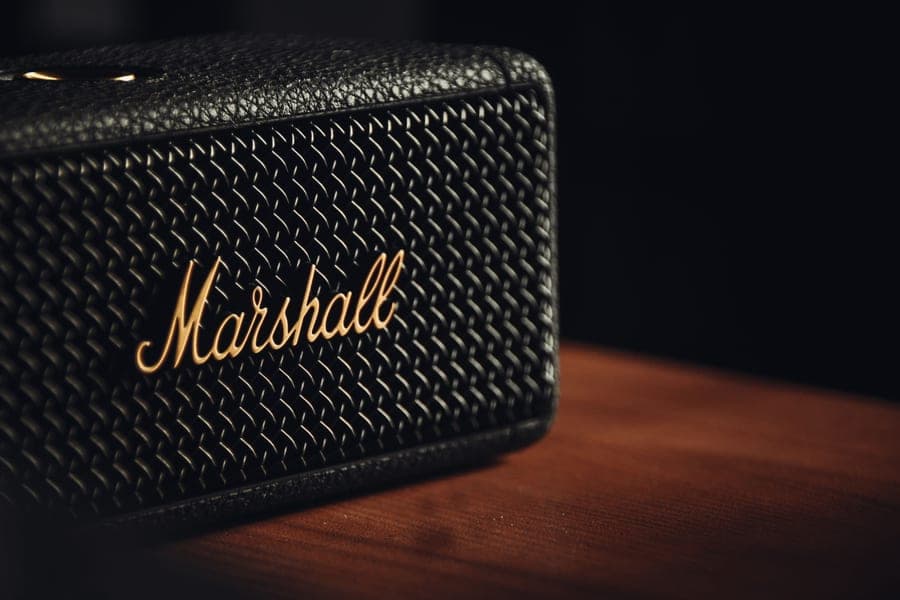 A rectangular fabric-wrapped Bluetooth speaker on a stone ledge