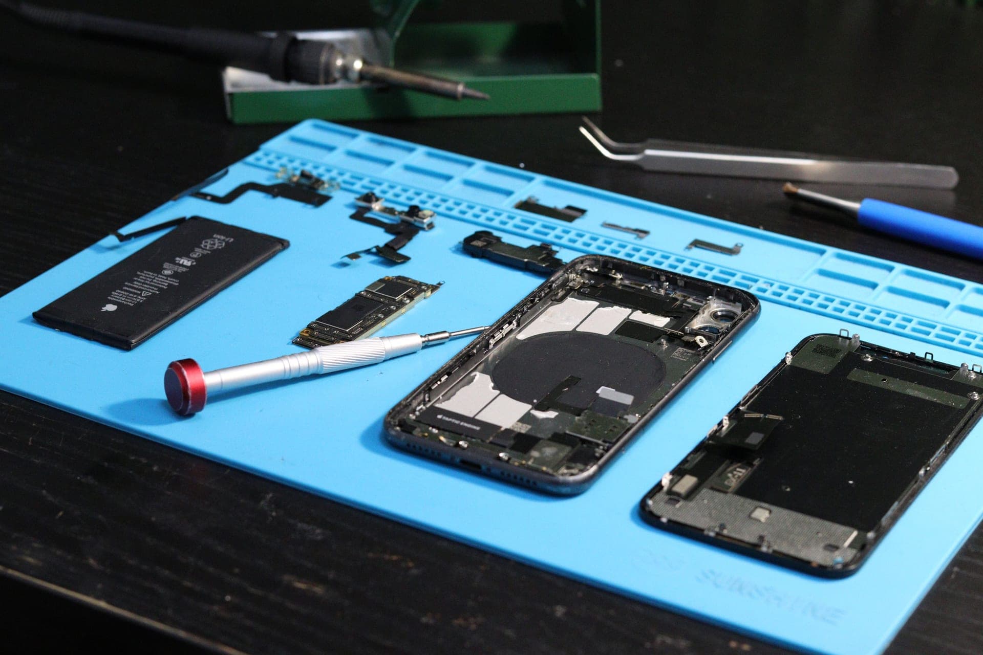 Disassembled electronics laid out on a repair mat with precision tools