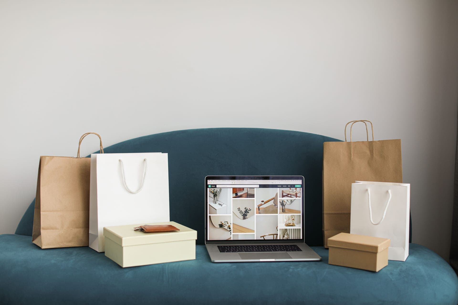 A laptop on a sofa surrounded by shopping bags and boxes