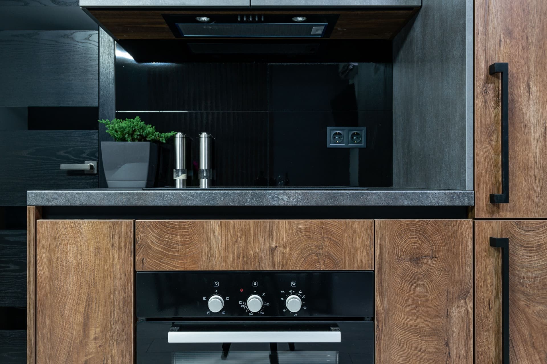 A modern kitchen interior with wooden cabinets, black fittings and a clear worktop