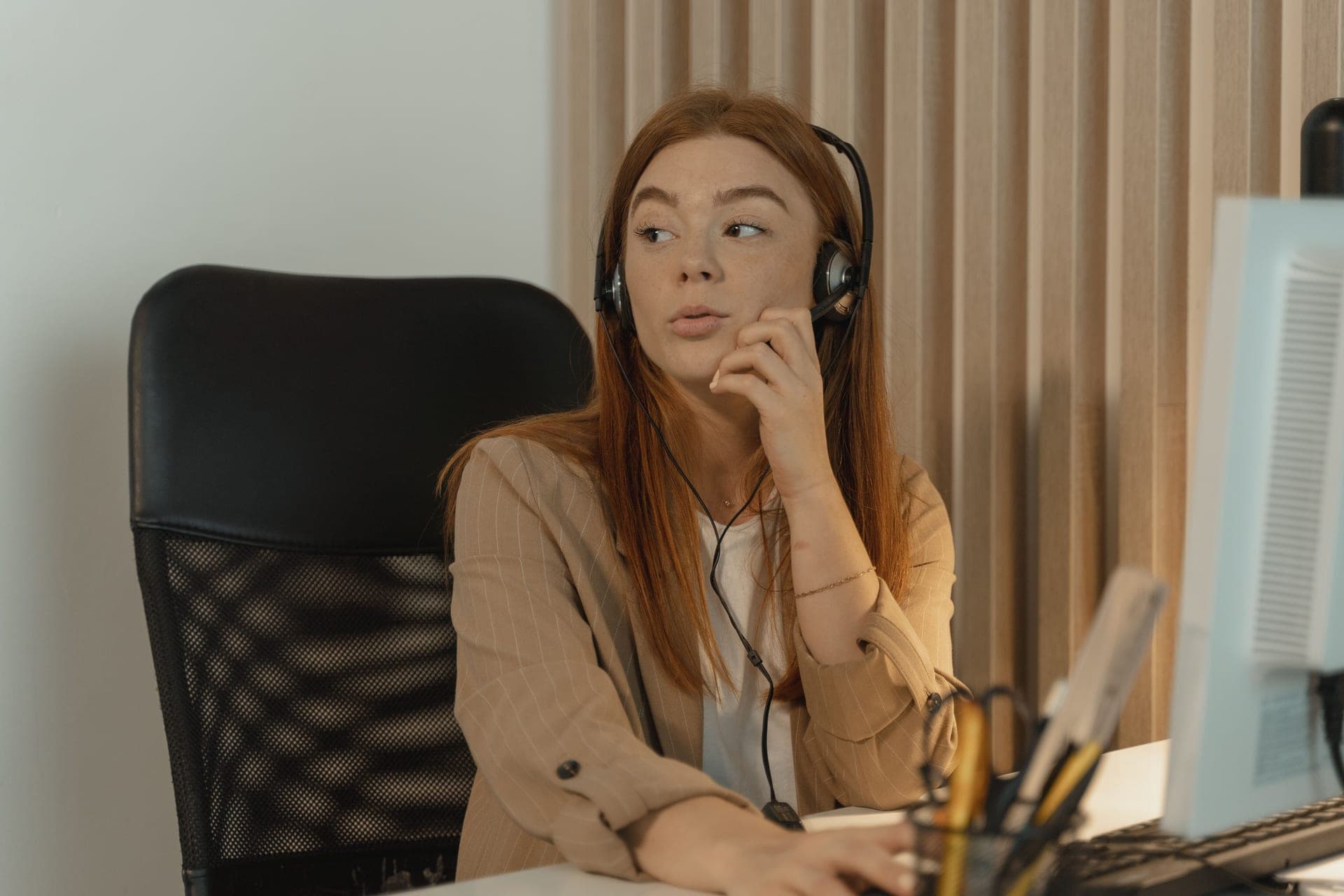 A person seated at a desk talking while wearing a headset