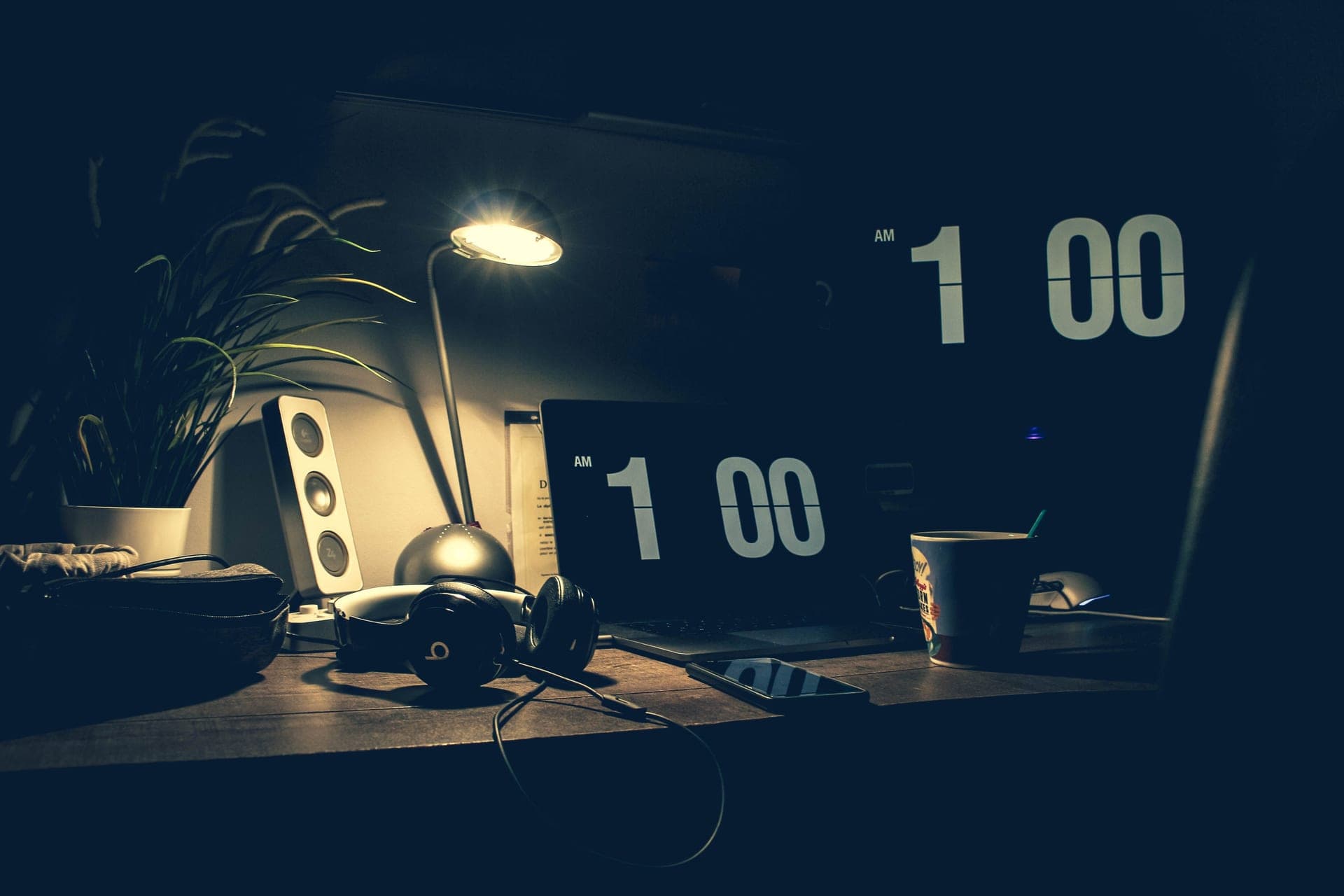 A dimly lit desk with a laptop, headphones and small speakers