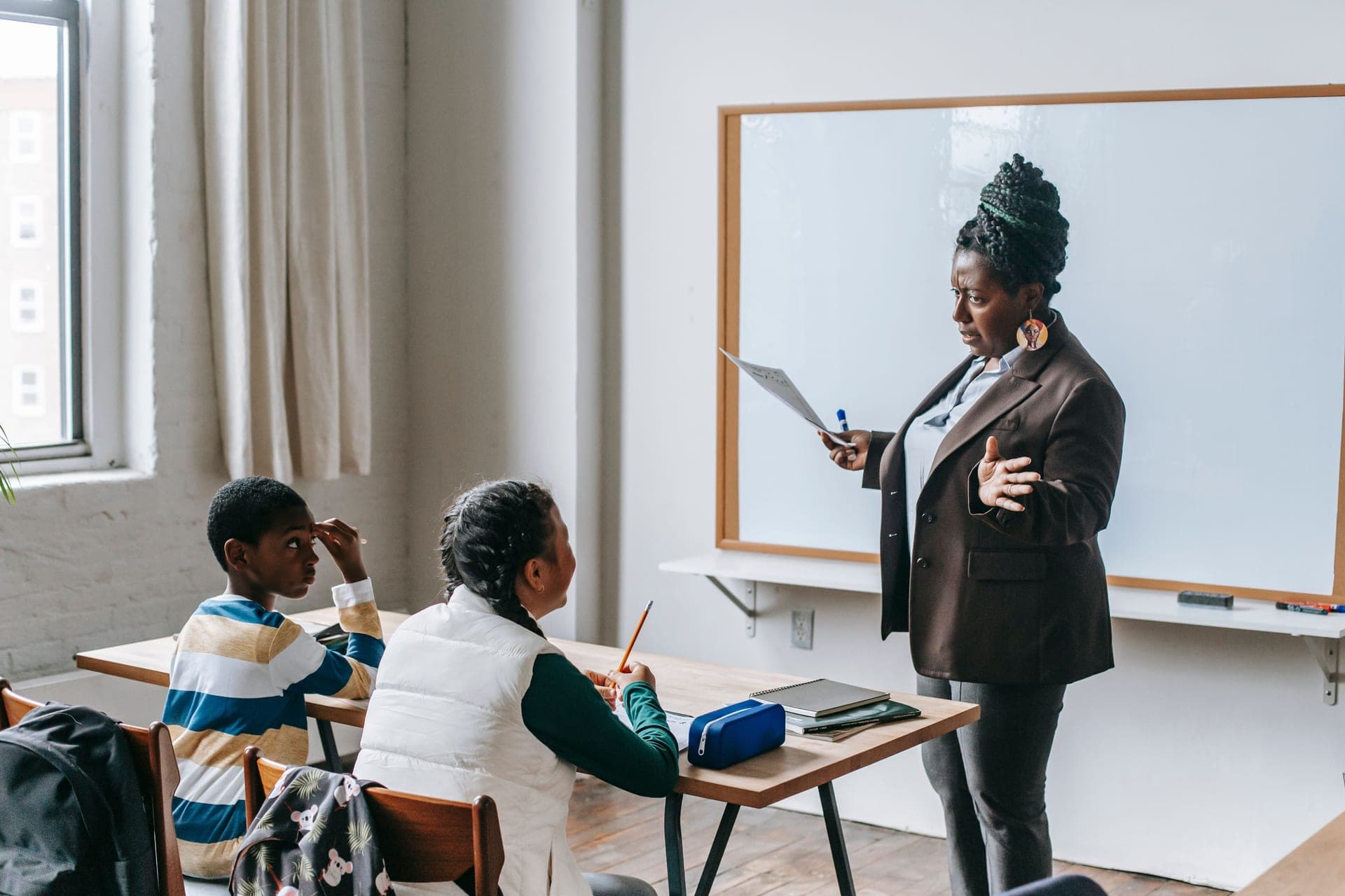 A teacher standing by a whiteboard explaining a lesson to pupils