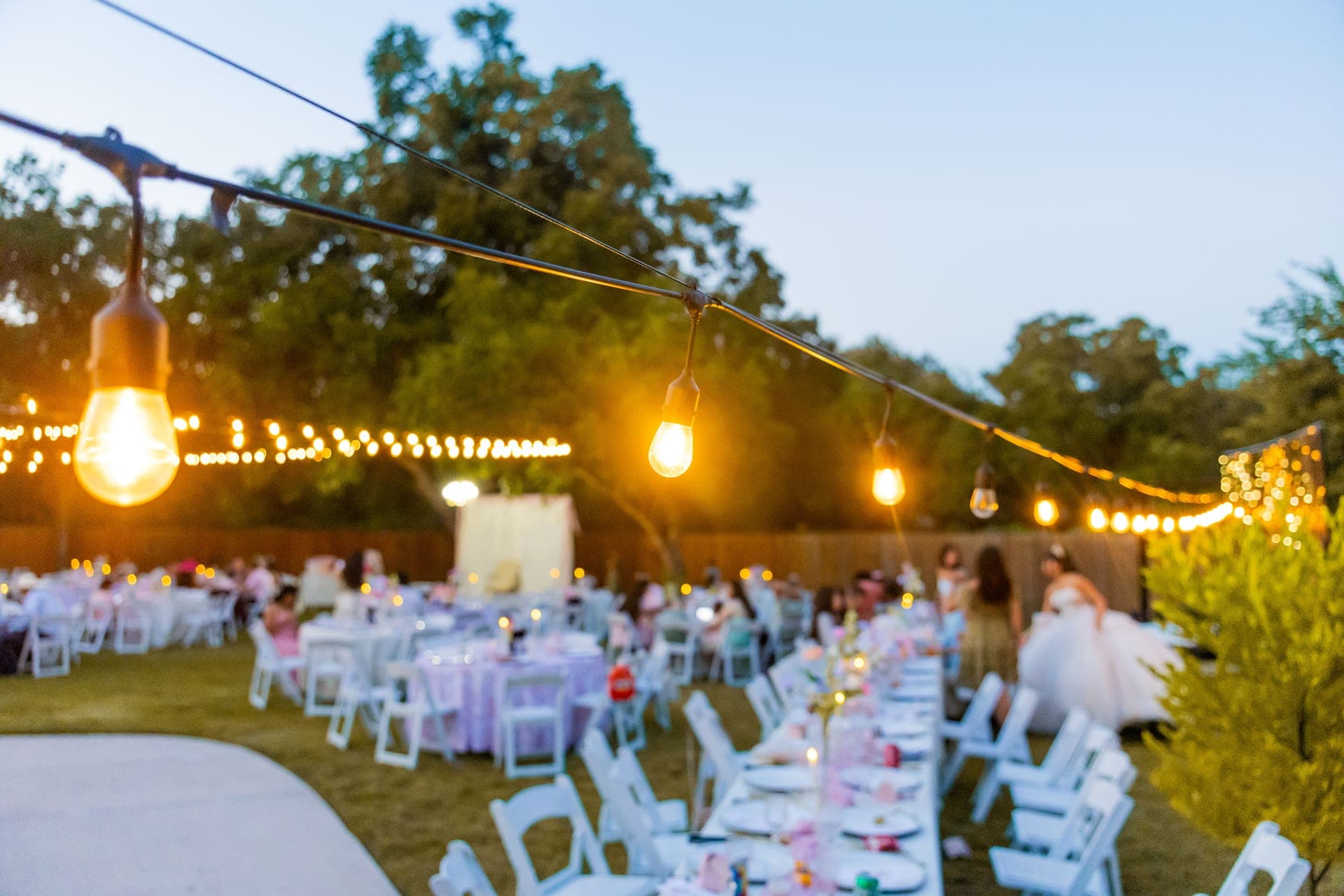 An outdoor wedding reception at sunset with tables under strung festoon lights